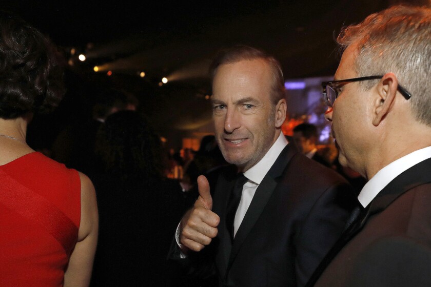 Bob Odenkirk, in suit and tie amid others at a nighttime venue, gives a thumbs up.