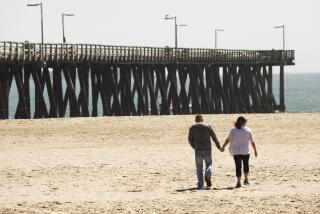 VENTURA, CA - APRIL 22: A couple hold hands as they walk along Hueneme Beach Wednesday which has a soft opening with restrictions as Ventura County on Saturday modified its stay-at-home order to permit some businesses to reopen and some gatherings to take place for the first time since the restrictions were issued to fight the spread of the coronavirus COVID-19. Ventura on Wednesday, April 22, 2020 in Ventura, CA. (Al Seib / Los Angeles Times)