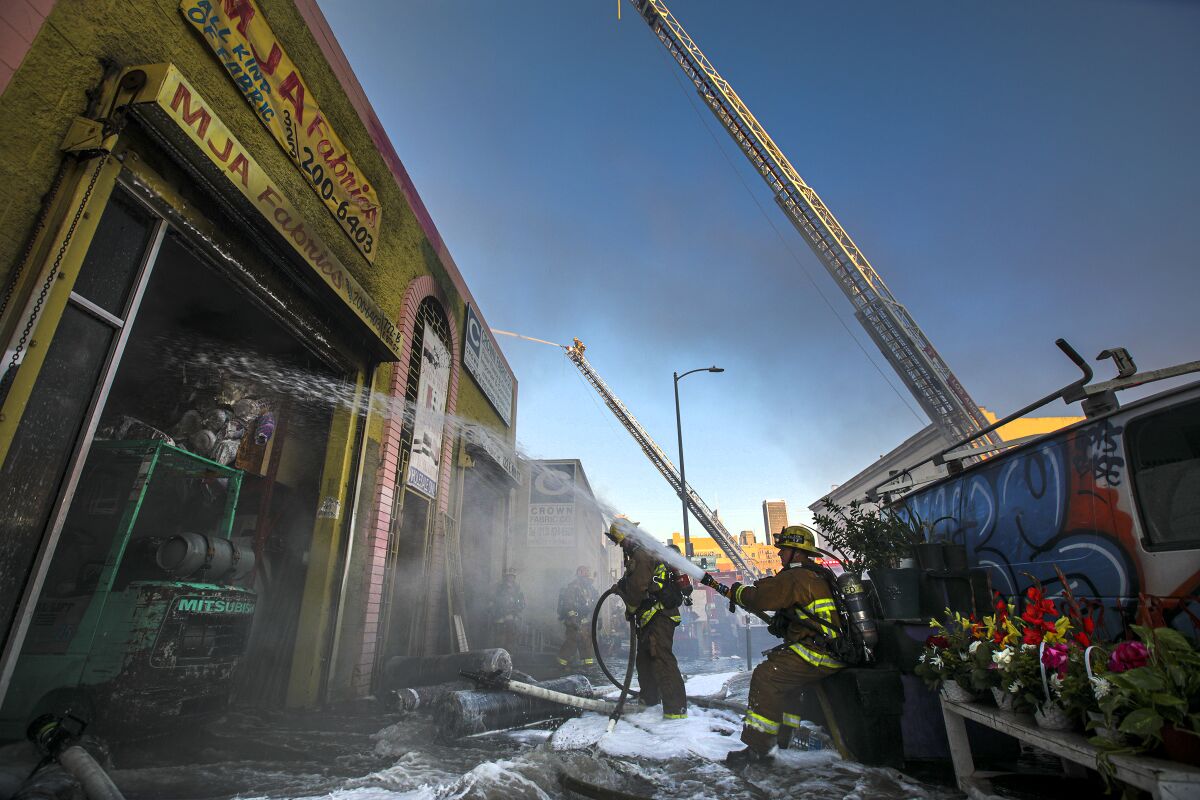 A firefighter trains a hose on the front of a Fashion District building.