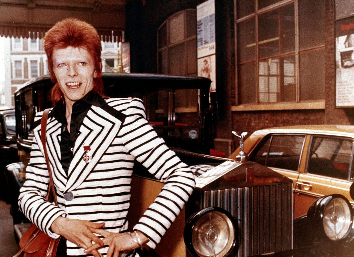 A man in a black and white striped suit poses in front of a vintage Rolls Royce