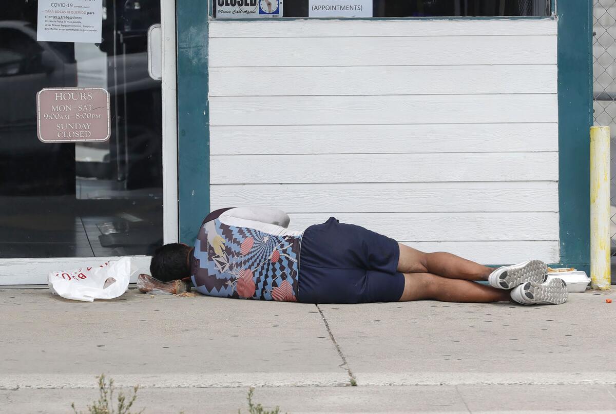 A mansleeps on the sidewalk in Costa Mesa. Orange County applied for funding from Project Homekey.