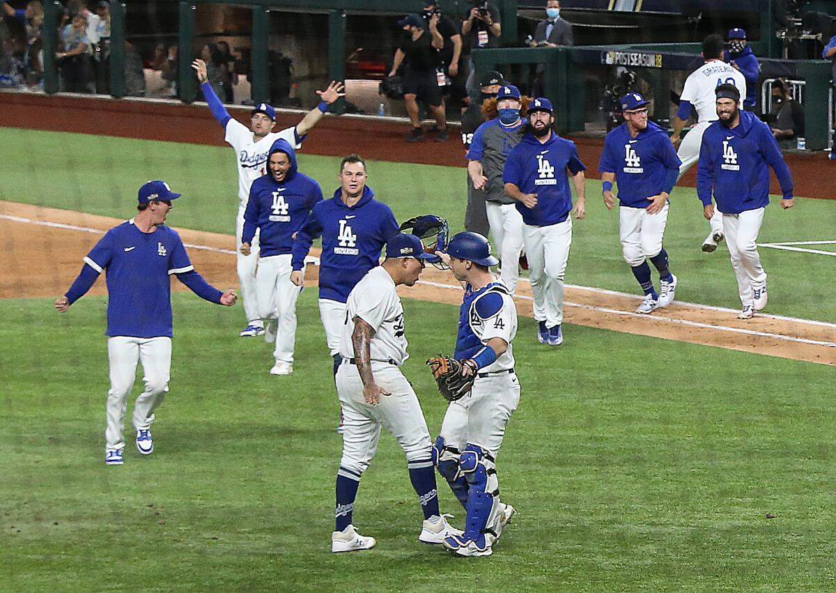 Dodgers pitcher Julio Urías is greeted by catcher Will Smith as teammates rush on the field.