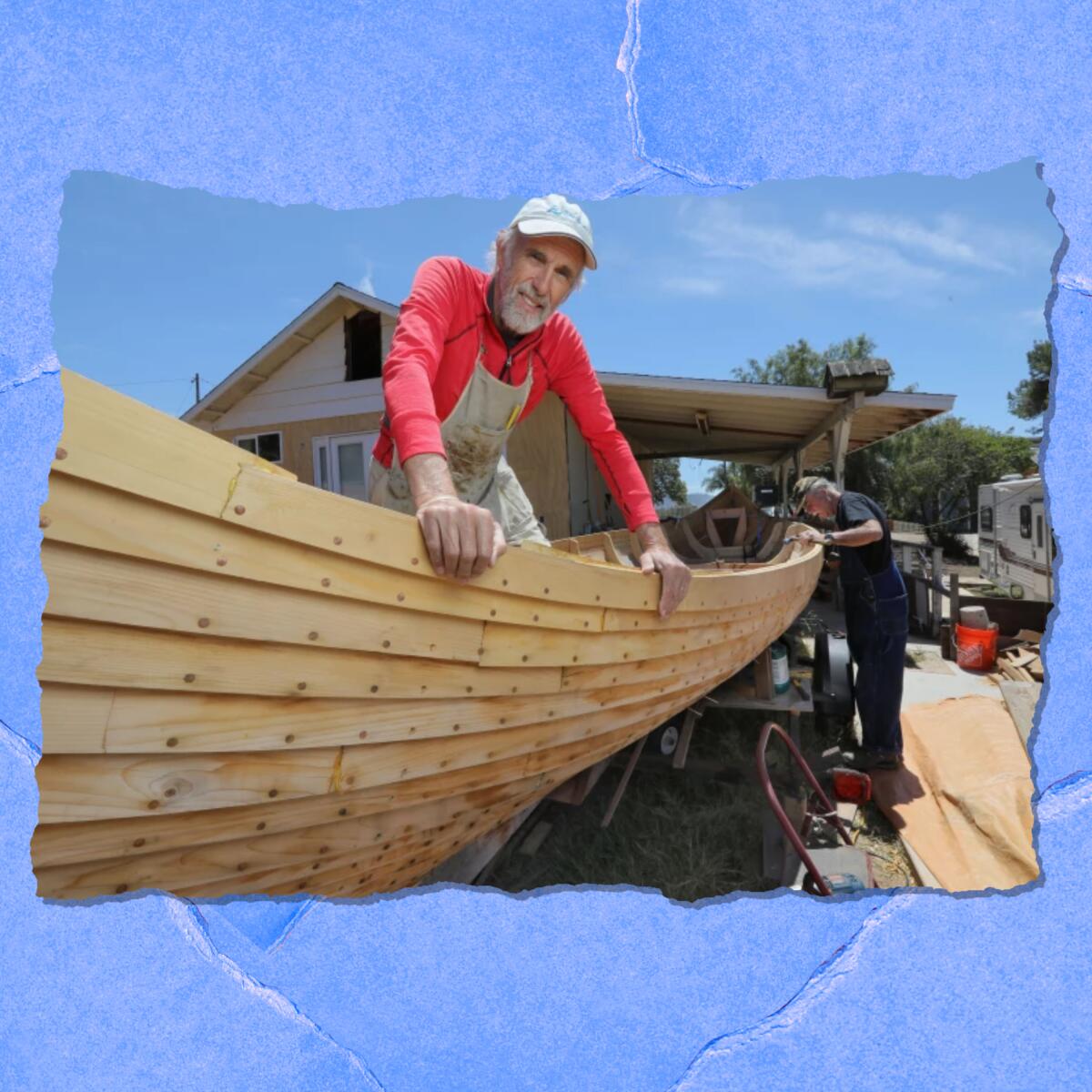 A man in a cap and work apron smiles from inside an unfinished boat.