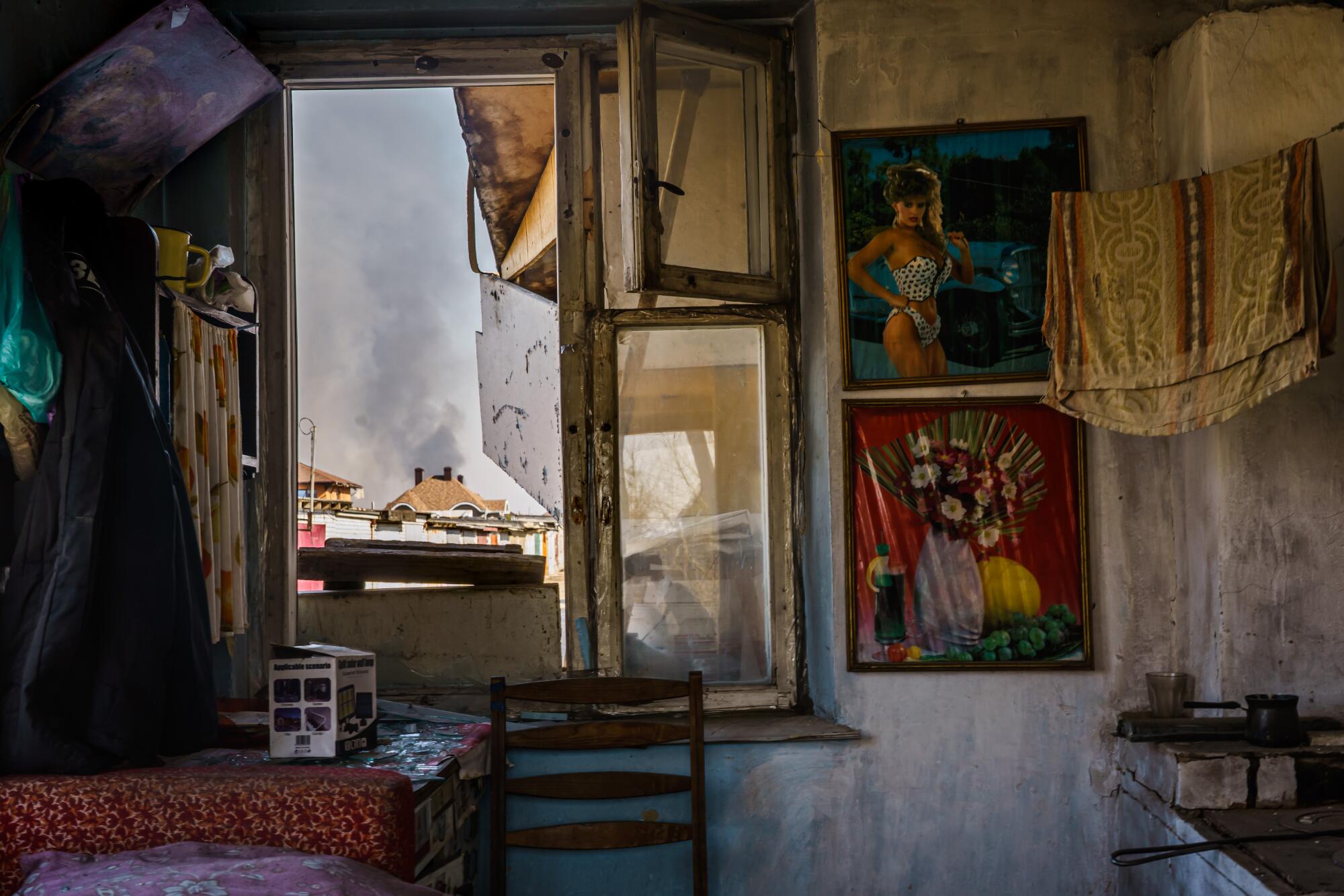 The inside of a room with a pinup girl poster on the wall and a window open showing smoke rising from a building.