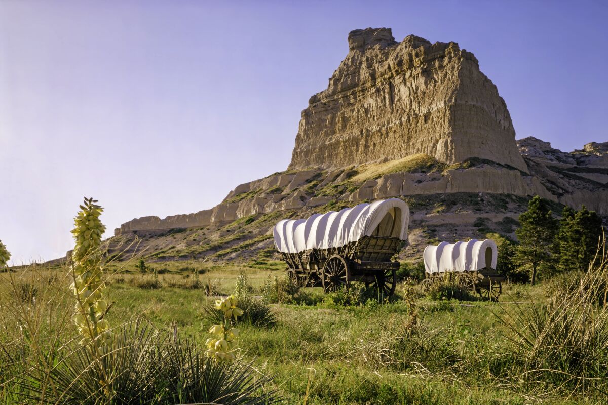 Covered wagons in front of rocky bluff at Scotts Bluff National Monument in Nebraska.
