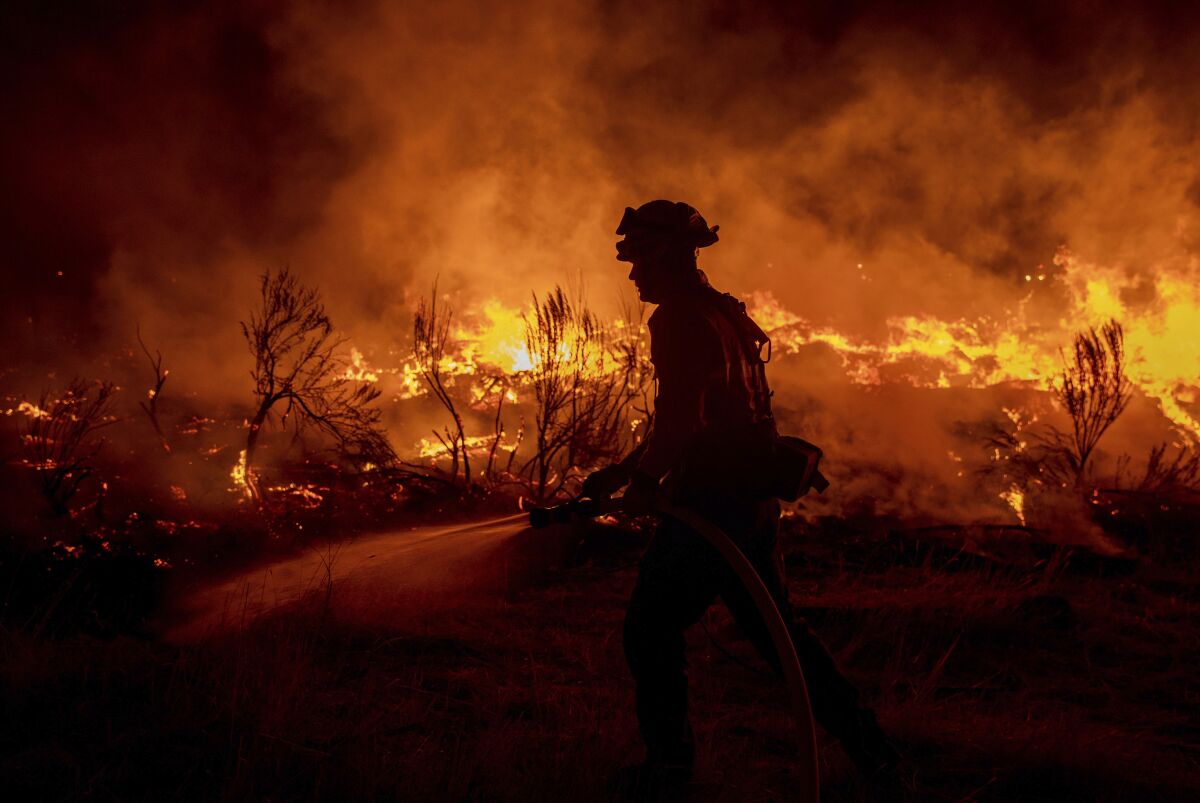 A firefighter hoses down flames amid a wildfire.