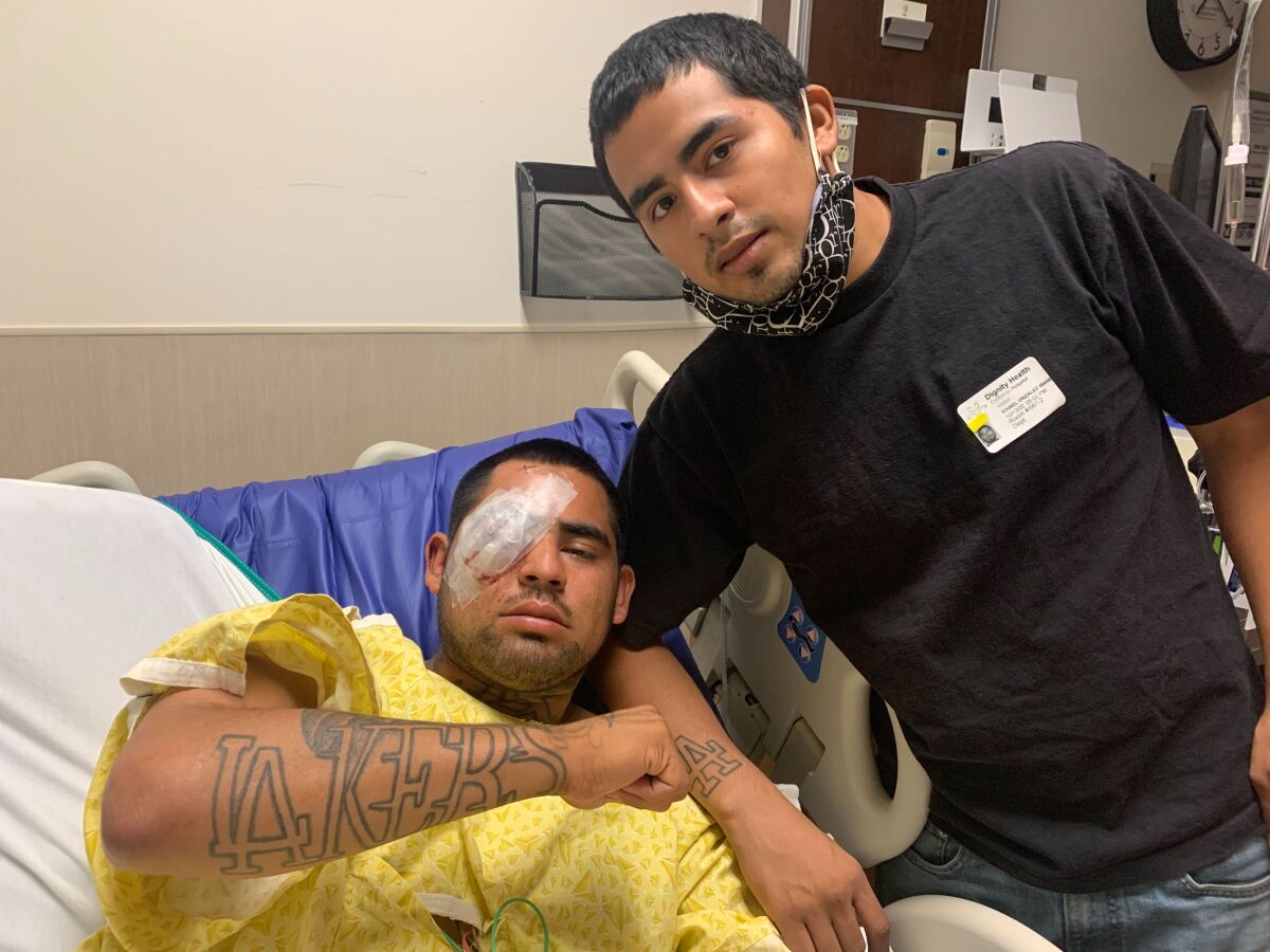 A man in a hospital bed with bandages over his right eye shows a Lakers tattoo on his forearm