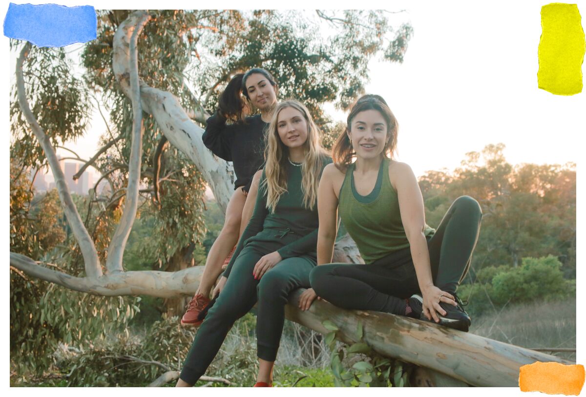 Three women in workout gear sit on a log.