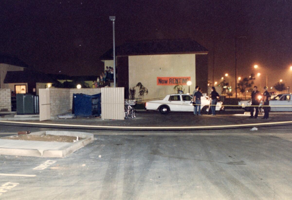 A dumpster blocked off by yellow police tape is near a building and cars at night.