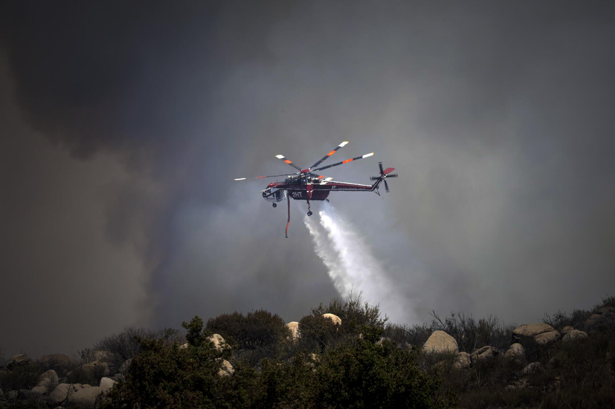 A helicopter drops water on a burning hillside. 