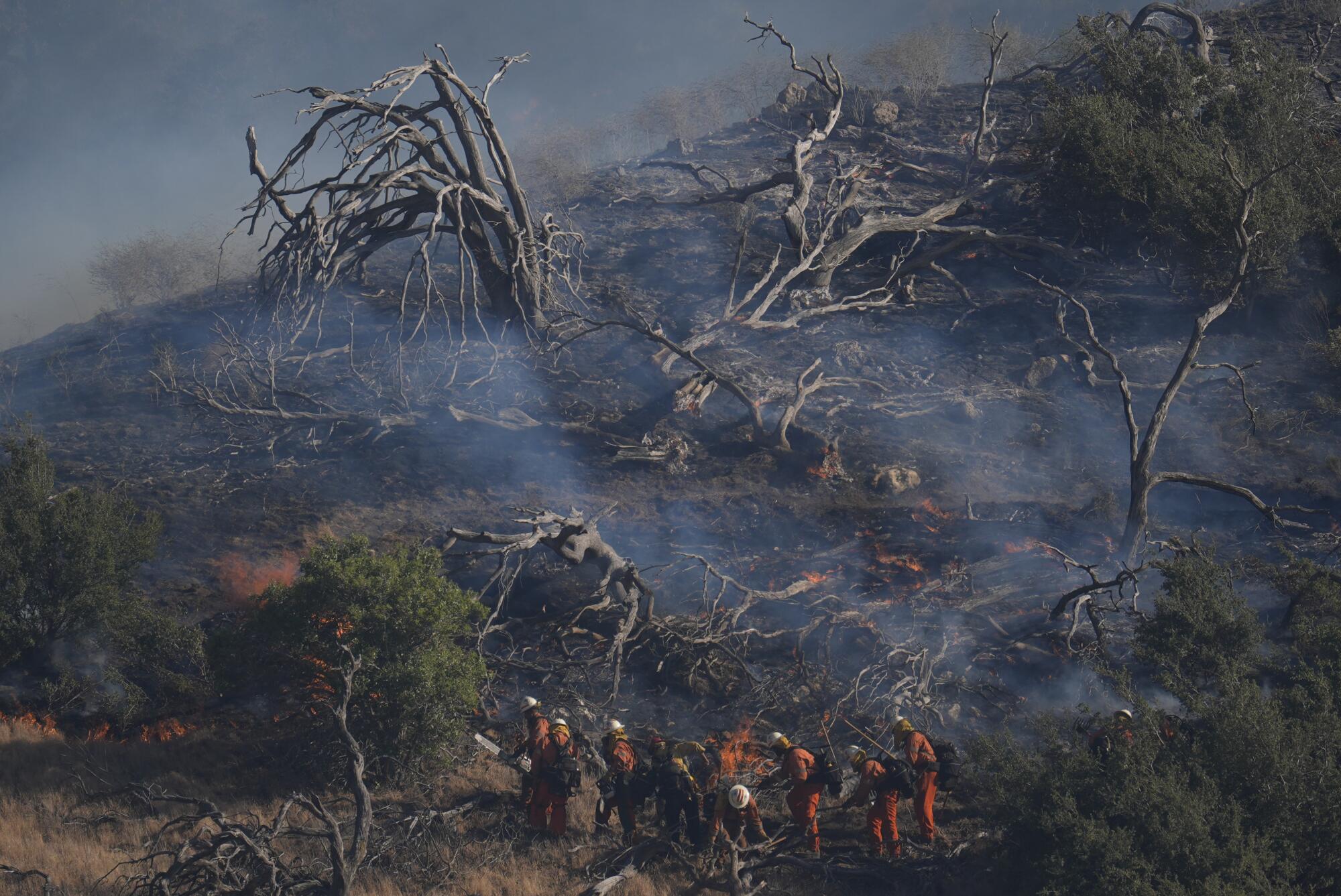 Firefighters work under a smoky hillside left by the Post Fire 