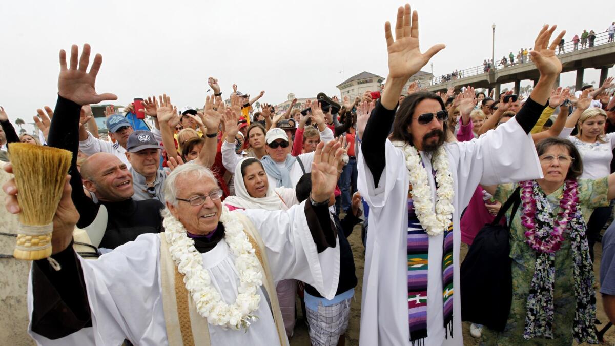 In 2010, the Rev. Christian Mondor, left, offers a prayer to surfers during the Blessing of the Waves ceremony in Huntington Beach.