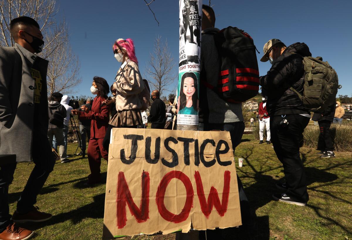 People attend a rally with a sign that reads "Justice Now" in the center. 