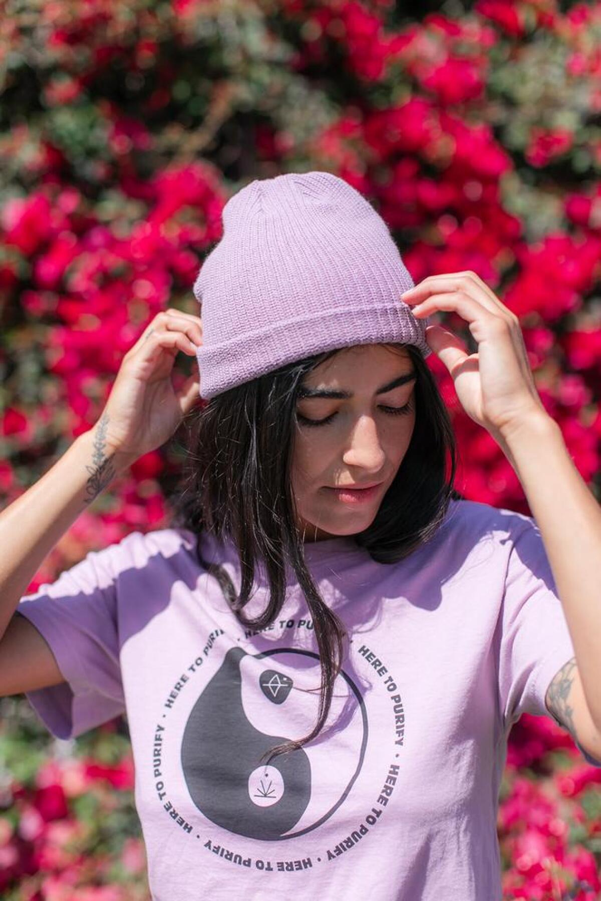 A woman wears a lilac-colored beanie and T-shirt.