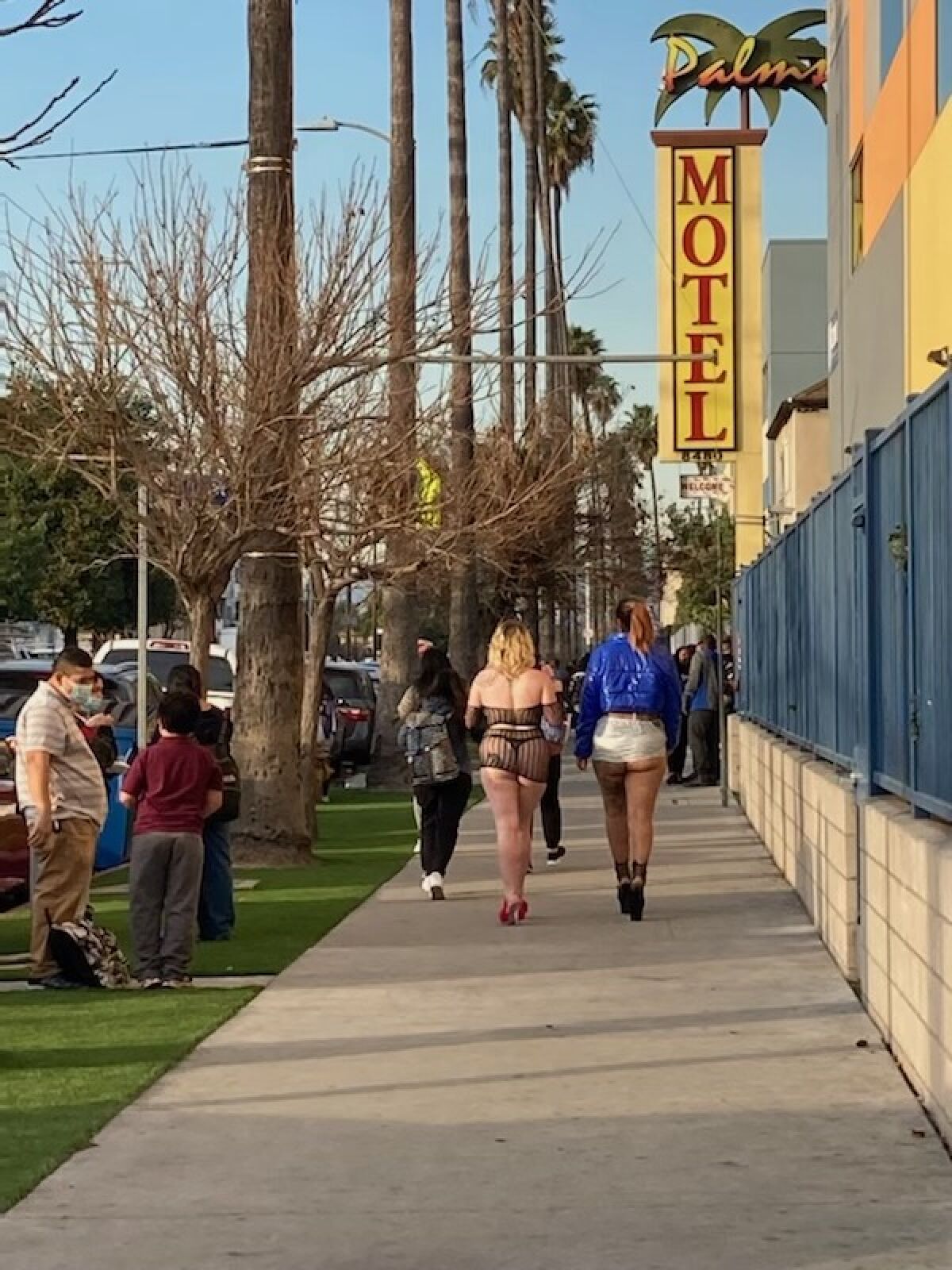 Two women in high heels walk past Palms Motel.