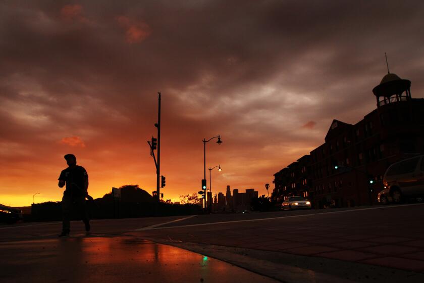 A passing storm gives way to a golden sunset as a pedestrian crosses the intersection of 1st Street and Boyle Avenue in Boyle Heights on Oct. 19, 2015. (Luis Sinco/Los Angeles Times)