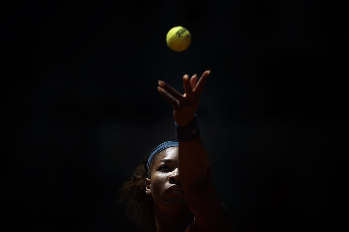 A woman tosses a tennis ball in the air