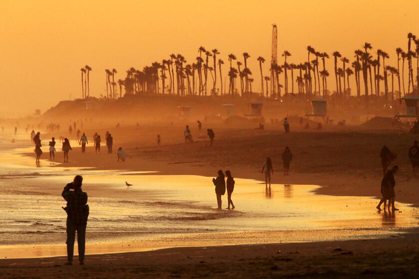 HUNTINGTON BEACH, CALIF. - JULY 12, 2023. Beachgoers take in the cooling mist of the ocean as the sun sets on Huntington Beach. Southern California weather is expected to get hotter in coming days as the region experiences the first significant heatwave of the summer. . (Luis Sinco / Los Angeles Times)