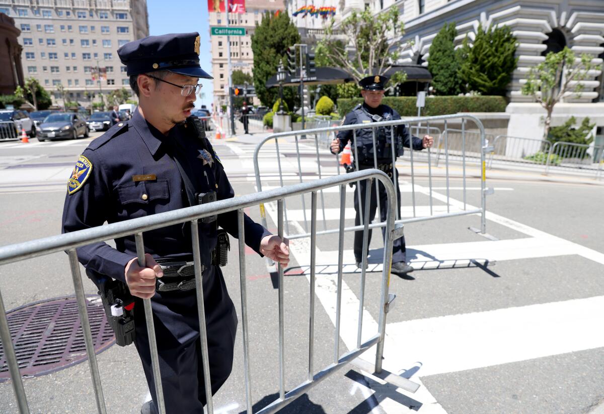 Two men in police uniform hold metal traffic barriers on a city street.