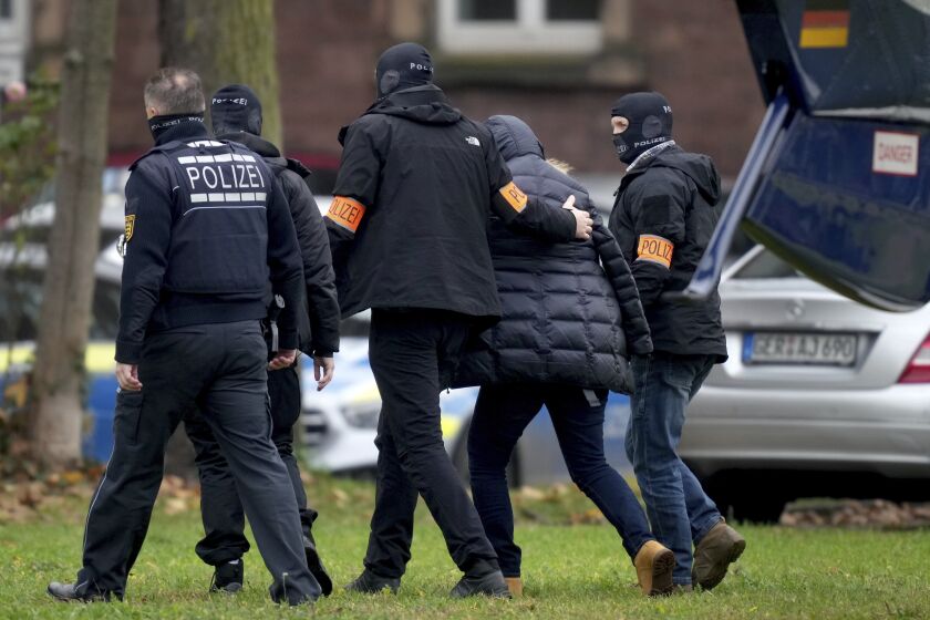 An suspect, second right, is escorted from a police helicopter by police officers after the arrival for a questioning at the federal prosecutor's office in Karlsruhe, Germany, Wednesday, Dec. 7, 2022. Thousands of police officers carried out raids across much of Germany on Wednesday against suspected far-right extremists who allegedly sought to overthrow the government in an armed coup. Officials said 25 people were detained. (AP Photo/Michael Probst)