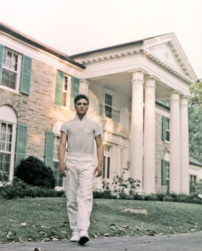 A young man walks in front of a mansion.