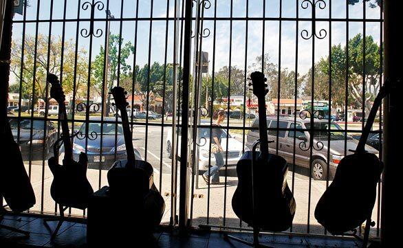 Used guitars hang in the window of a pawnshop in downtown Baldwin Park. City leaders this year enacted a moratorium on new payday loan and check-cashing stores. A project of mixed-income housing, theaters and mainstream restaurants such as Claim Jumper, Applebees and Chilis is in the works.