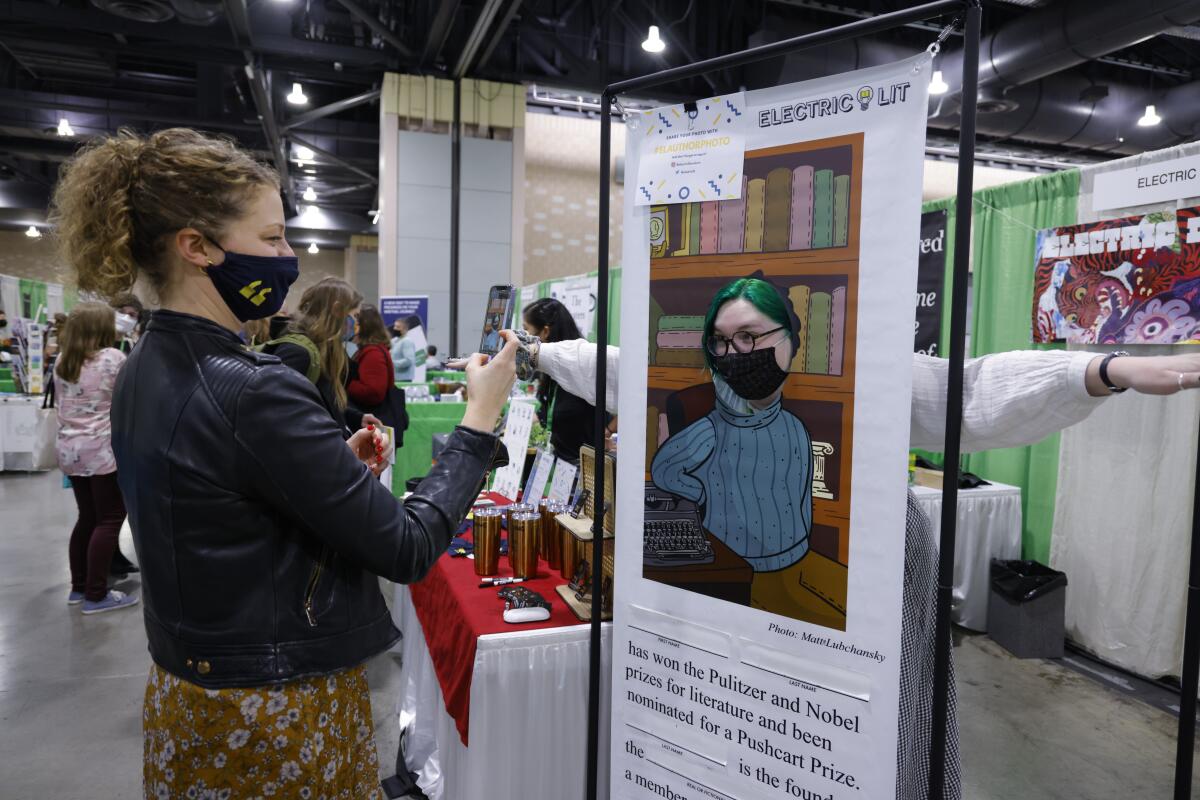 A masked woman takes a photo of a display at a conference.