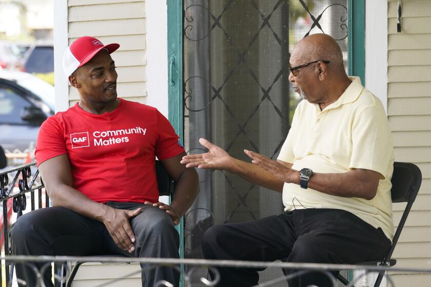 Actor Anthony Mackie, left, talks with resident Joe Capers, as he works with GAF Roofing Academy students who were volunteering to replace Capers' roof, in New Orleans, Tuesday, Sept. 12, 2023. (AP Photo/Gerald Herbert)