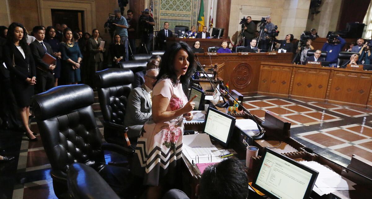 A woman speaks in City Council chambers with several people around her.