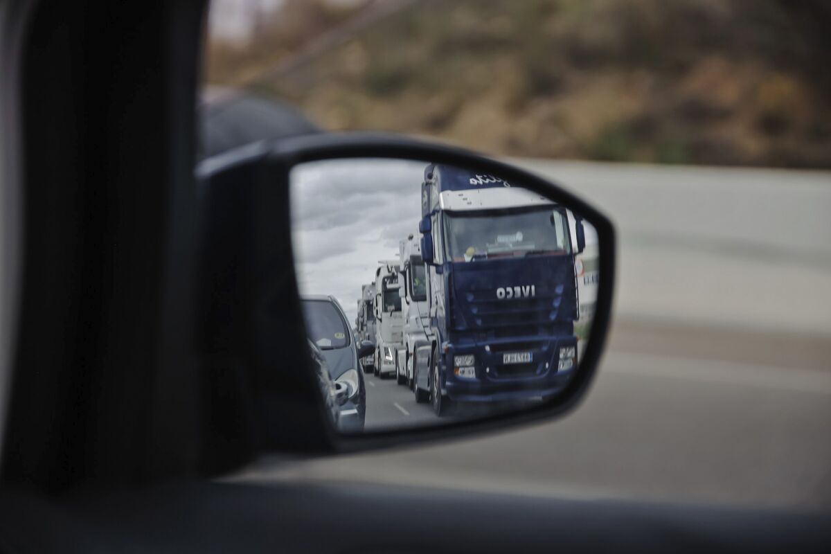 A long line of trucks driving slowly are reflected in a wing mirror of a car during a truckers strike in Torrejon de Ardoz, just outside of Madrid, Friday March 18, 2022. More than 23,000 Spanish police in patrol cars and helicopters are escorting convoys of trucks along the country's highways and holding back picketers as authorities seek to keep supply chains working amid a truckers' strike over high fuel prices and other grievances. (Carlos Lujan/Europa Press via AP) **SPAIN OUT**
