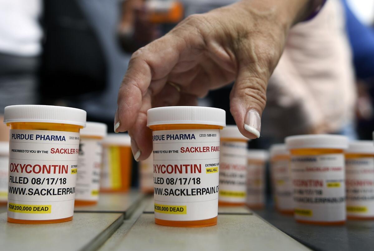 Rows of Oxycontin pill bottles on a table with people standing in the background.