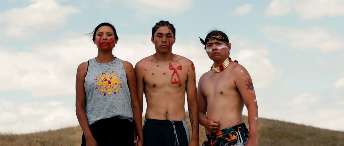 Three Indigenous persons in face makeup pose for the camera.