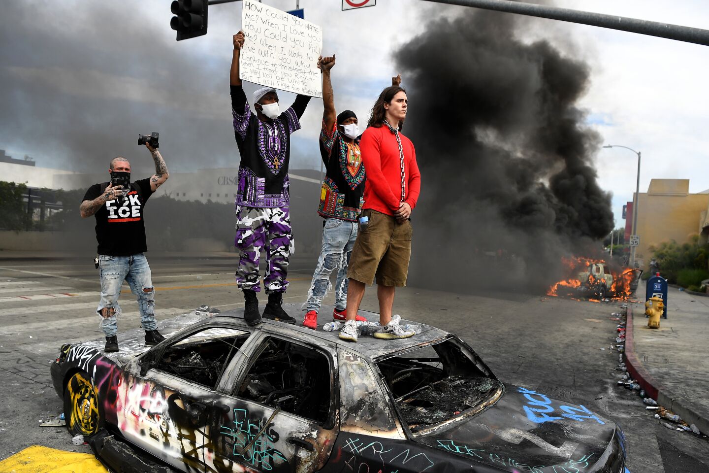Protesters stand on top of a burned LAPD cruiser.