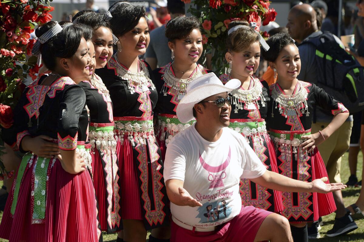 A man in a white hat, white T-shirt and red shorts poses with a group of women in red-and-black costumes 