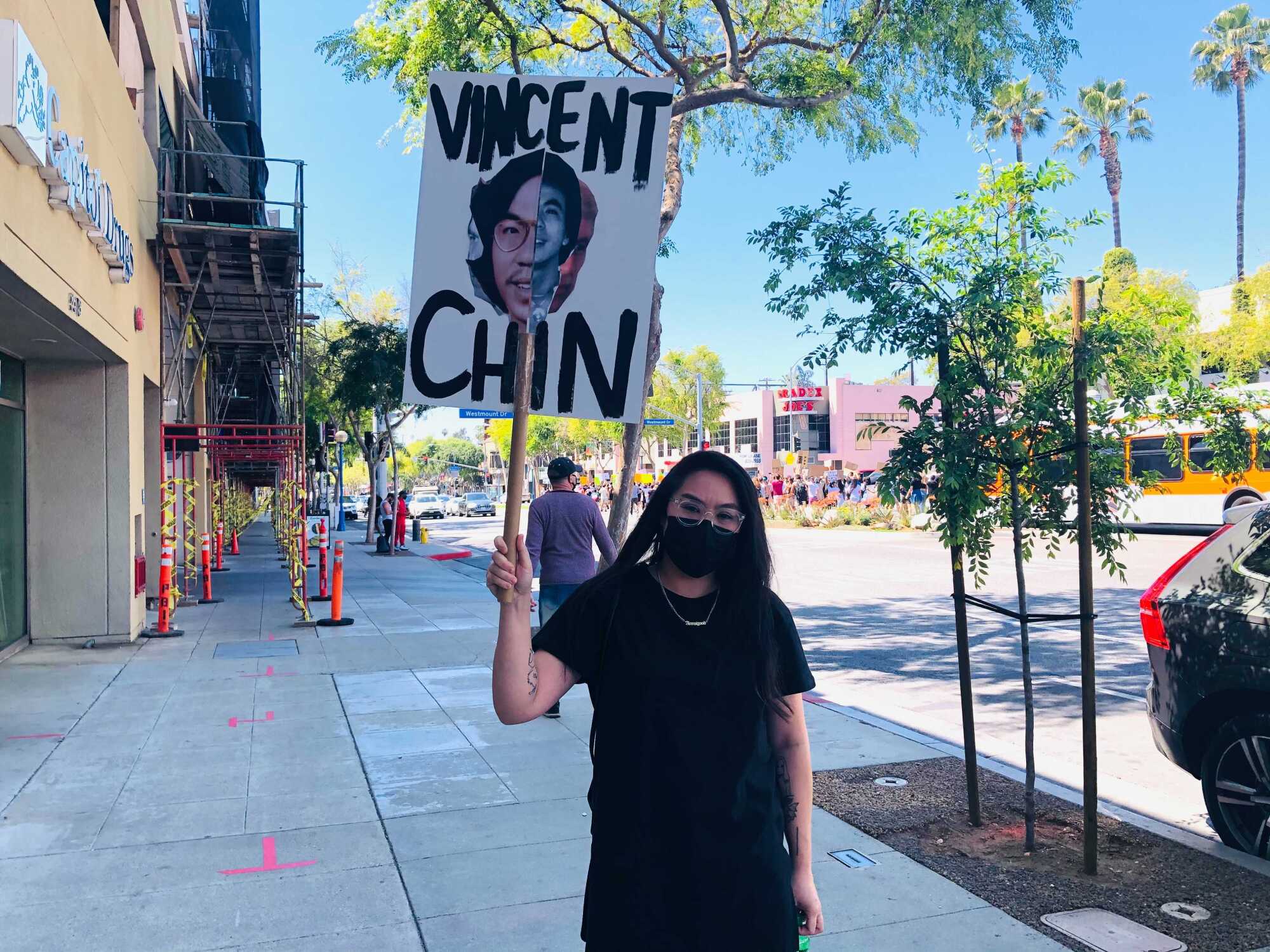 Artist Ann Le stands on a sidewalk holding a sign with a collage she created of Vincent Chin.