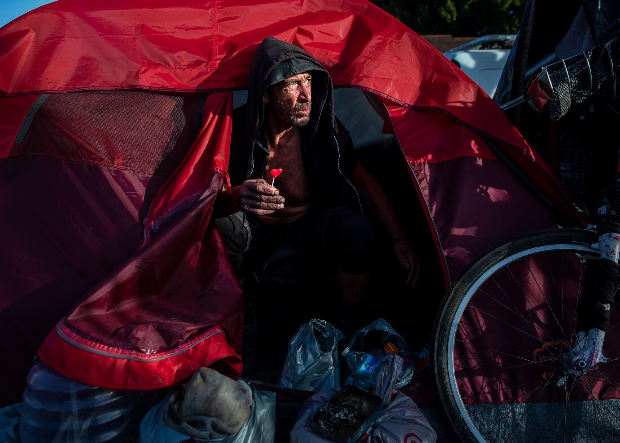 A man, holding a red, heart-shaped lolly pop, emerges from an entry of a red tent. 