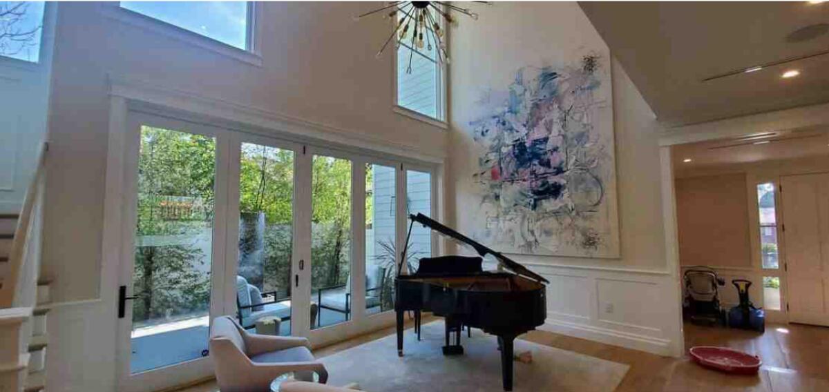 A grand piano sits in a high-ceilinged living room with large glass doors opening to a patio