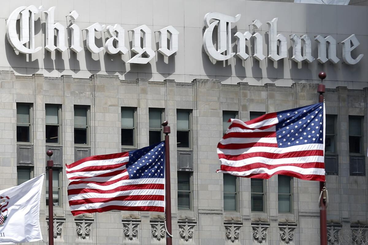 With three flags flying in the foreground, the Chicago Tribune name is seen on the neo-Gothic skyscraper in Chicago.