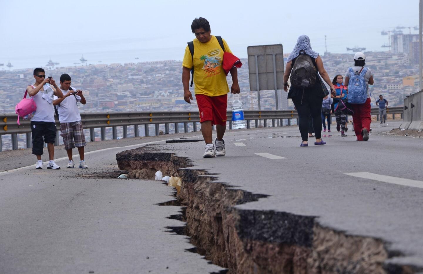 People walk along a cracked road in Iquique, in northern Chile, a day after a powerful earthquake hit Chile's Pacific coast, killing at least six people and generating tsunami waves that might ripple as far as Indonesia.