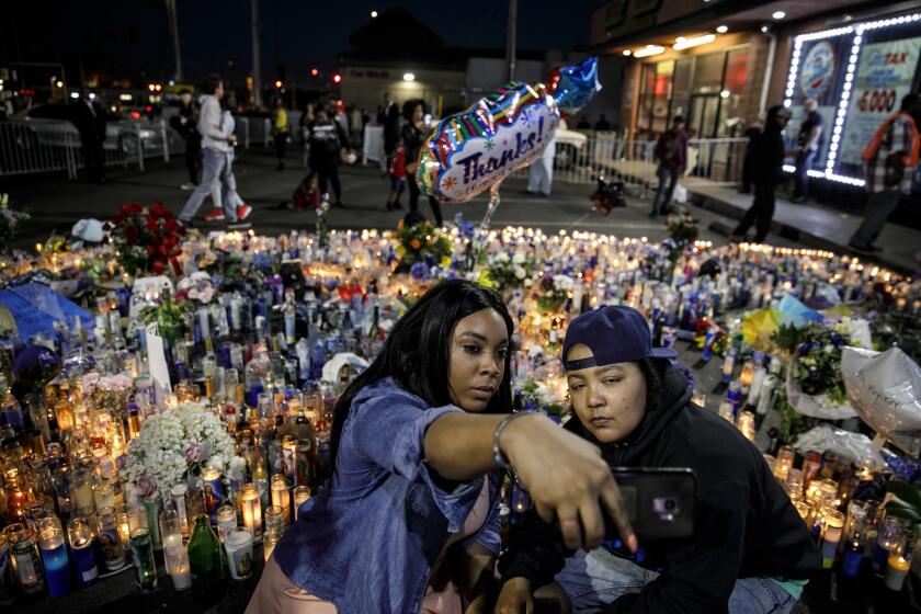 Kiara Career, left, and Tadow McReynolds, from Minneapolis, take a selfie at the Nipsey Hussle memorial outside his Marathon Clothing store in Los Angeles.