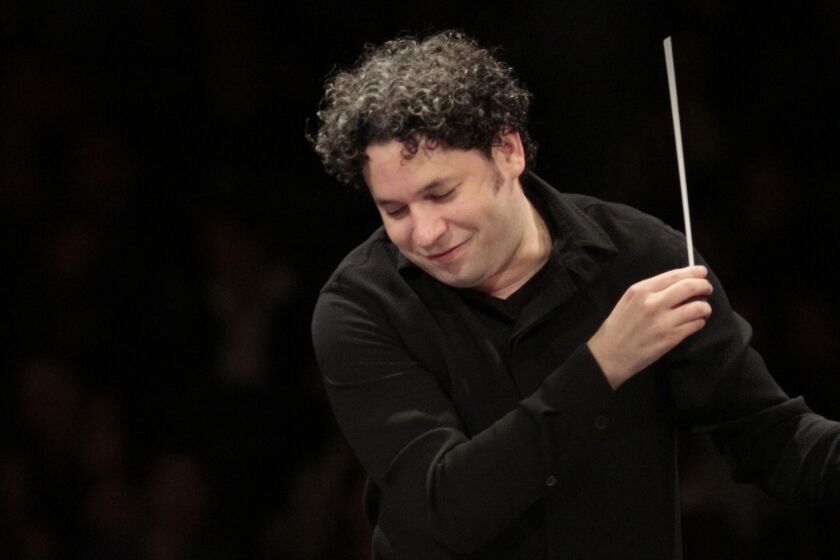 A maestro with curly black hair wearing a black collared shirt and conducting