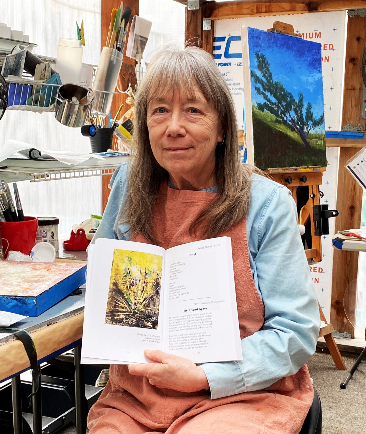 Poway artist Doris Bertch in her studio holding “Summation 2021-2022 Fourteenth Annual Anthology of Art and Poetry.”