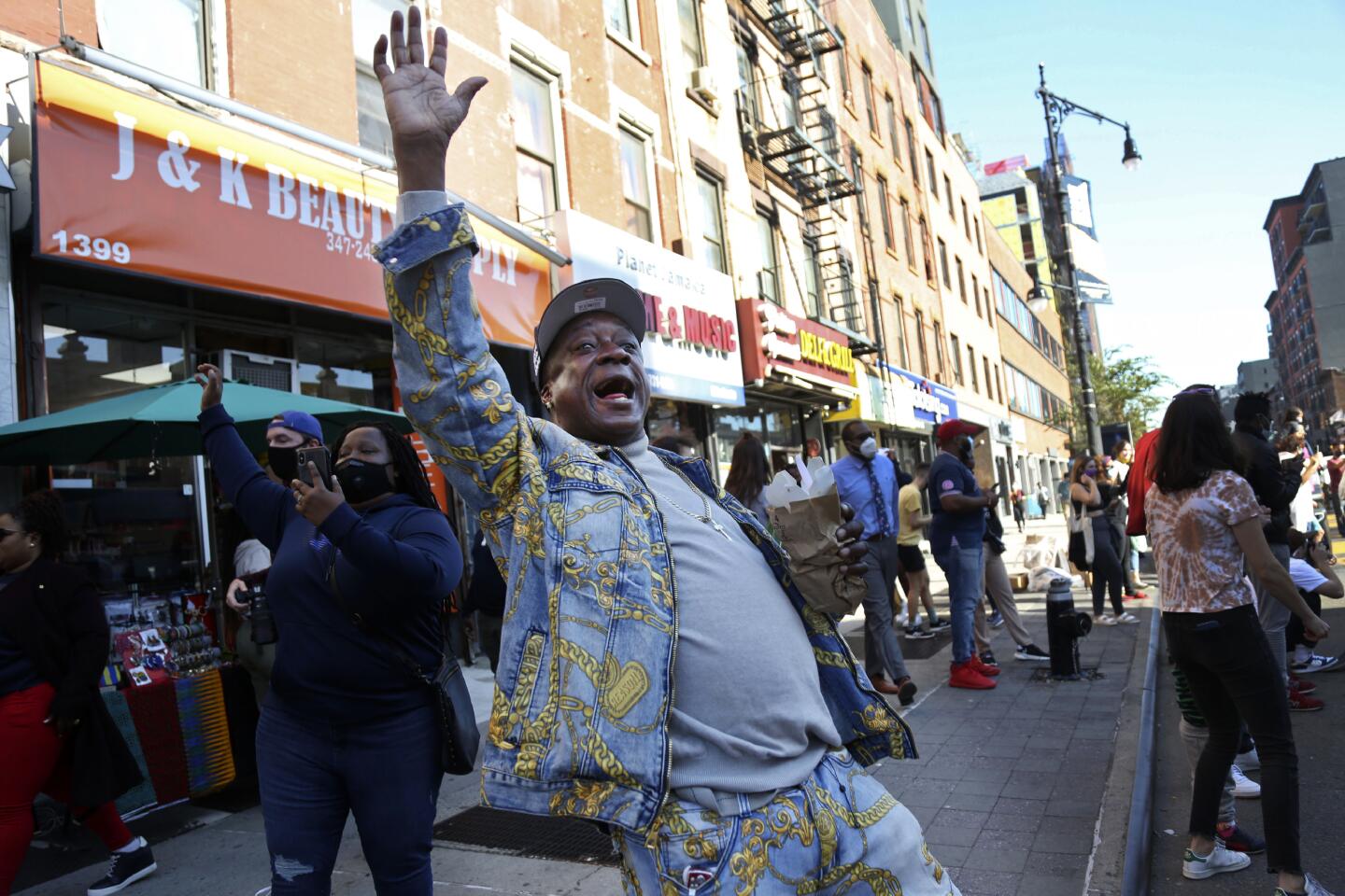 Marcel Cothron sings "Na na na na, hey hey goodbye" with a large crowd gathered on Fulton Street in the Brooklyn borough of New York, to celebrate Joe Biden's victory over President Donald Trump, Saturday, Nov. 7, 2020. (AP Photo/Jessie Wardarski)