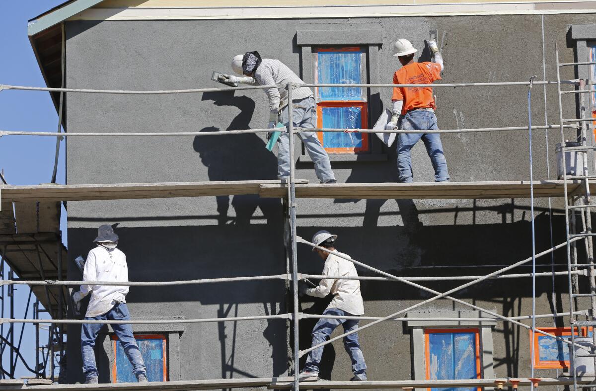 Four masons stand on a scaffolding as they put a coat of stucco on a two-story house 