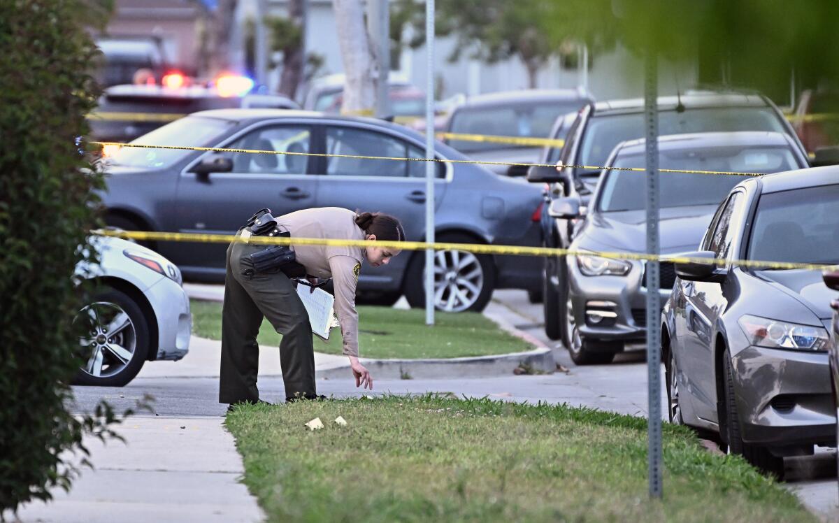 A sheriff's deputy bends over to pick something up behind yellow crime scene tape.