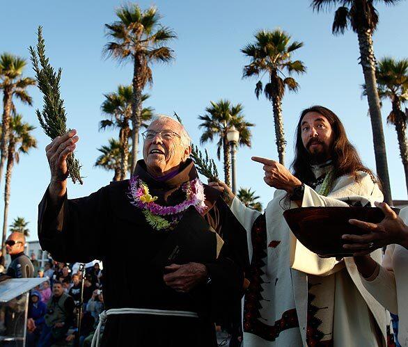 Father Christian Mondor, left, of Sts. Simon and Jude Catholic Church in Huntington Beach and Father Matt Munoz of St. Irenaeus Catholic Church in Cypress took long stems of rosemary, dipped them in a large wooden bowl filled with holy water and sprinkled the crowd. After the service, Mondor went body surfing and Munoz rode a long board.