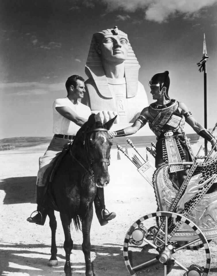 1955: Charlton Heston, left, rides on horseback while shaking hands with Yul Brynner, who stands in a chariot before filming the chase sequence on the set of director Cecil B. DeMille's film, "The Ten Commandments."