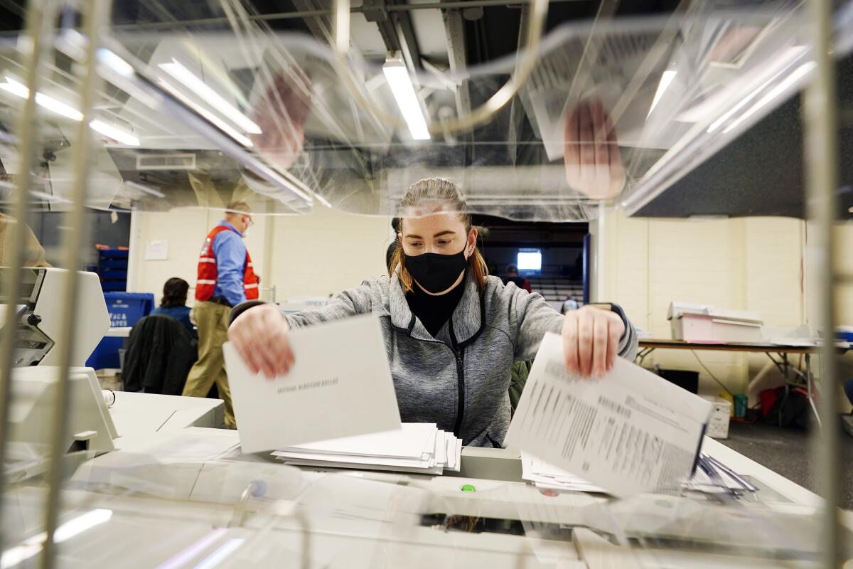 A woman wearing a mask sorts through mail-in ballot envelopes