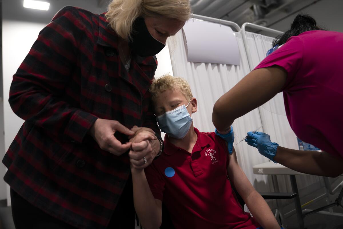 A woman holds a boy's hand as a health worker administers a shot