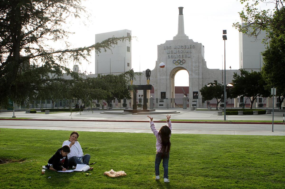 Crishell Calvillo, 5, plays catch with herself as her grandmother Leticia Calvillo, helps her cousin Anthony Gomez, 7, do his homework, near the Los Angeles Memorial Coliseum, seen in background on March 5, 2012.